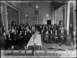 Gruppe kvinner og menn i festpyntet sal, mann med laurbærkra