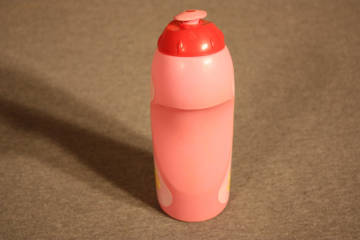 Plastflaske  med skrukorkog drikketopp. Flaska er forma til handgrep. Pålimt etikett med brystbilete av ei Barbiedokke i midten. Skrive Synne E. med tusj under botnen.