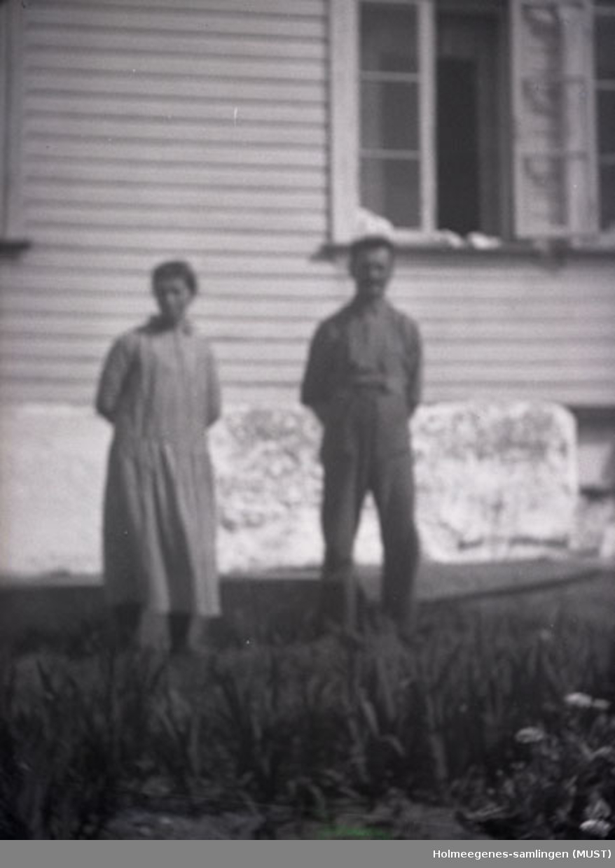 En kvinne og en mann oppstilt foran et bolighus. Antatt samme sted og tidspunkt på ST.K.HE 2010-011-0096 til -0100.