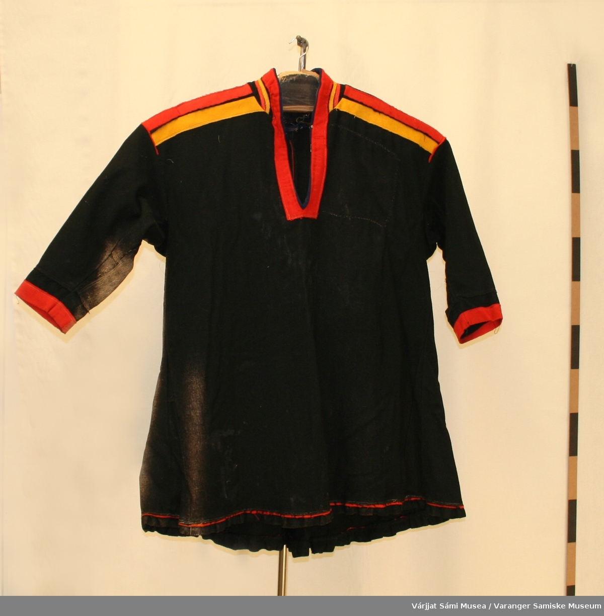 En svart herrekofte av klede, sannsynligvis fra Polmak. Den har en blåprikket lomme på venstre side foran. På høyresiden er kofta og ermet falmet. Kofta kan også være fra Utsjok/Nuorgam.