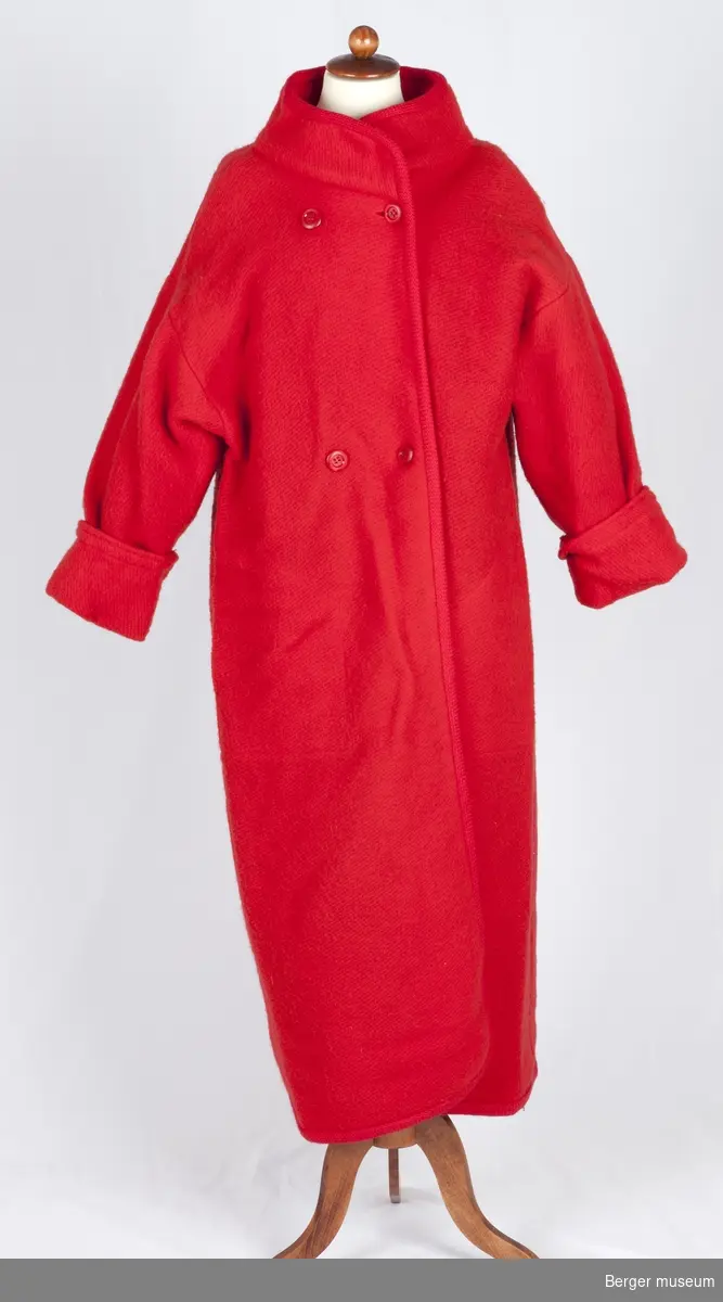 Lang rød kåpe med store røde knapper, krage, lommer og oppbrettede ermer. Det er sydd på skulderputer i skumgummi med silketrekk.
Møllsikret. 