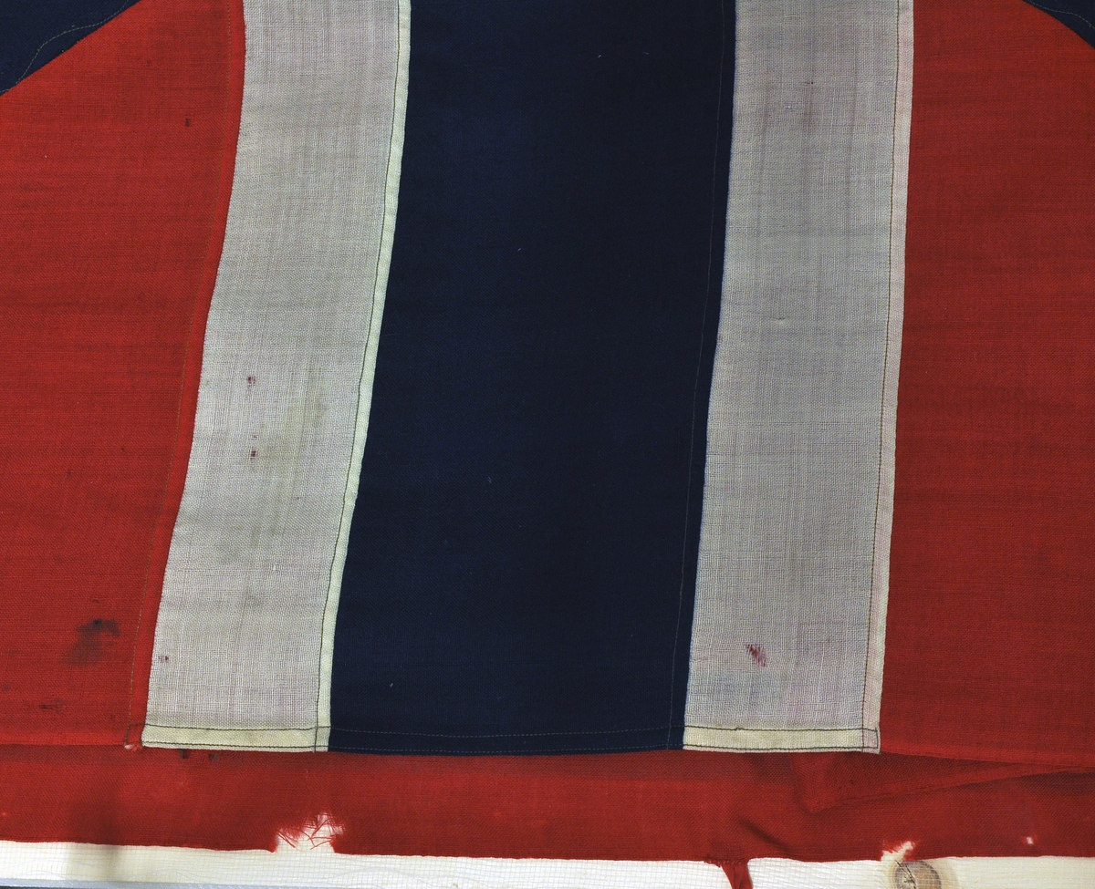 Norsk flagg med unionsmerke ("sildesalat). Unionsmerket er applikert på en rød rute øverst i høyre hjørne.
Det er påmontert  kanalgang(5,5cm) for feste av tau. Inne i kanalgangen er det antakeligvis tau av hamp. I enden av kanalgangen er det montert på en festeanordning av metall.