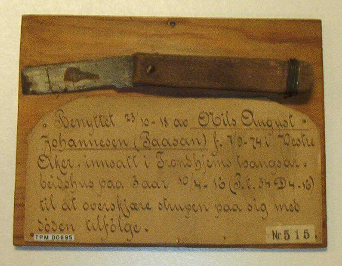 Hjemmelaget kniv med brukket blad, montert på treplate sammen med en papirlapp med håndskrevet tekst.