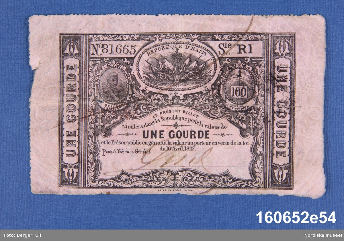 Sedel utgiven av La Republique d'Haiti, 1 gourde. Enligt lagen från den 16 april 1827, nr 81665 serie R1.
Anm.: Två ovala stämplar på baksidan, en svart och en röd.