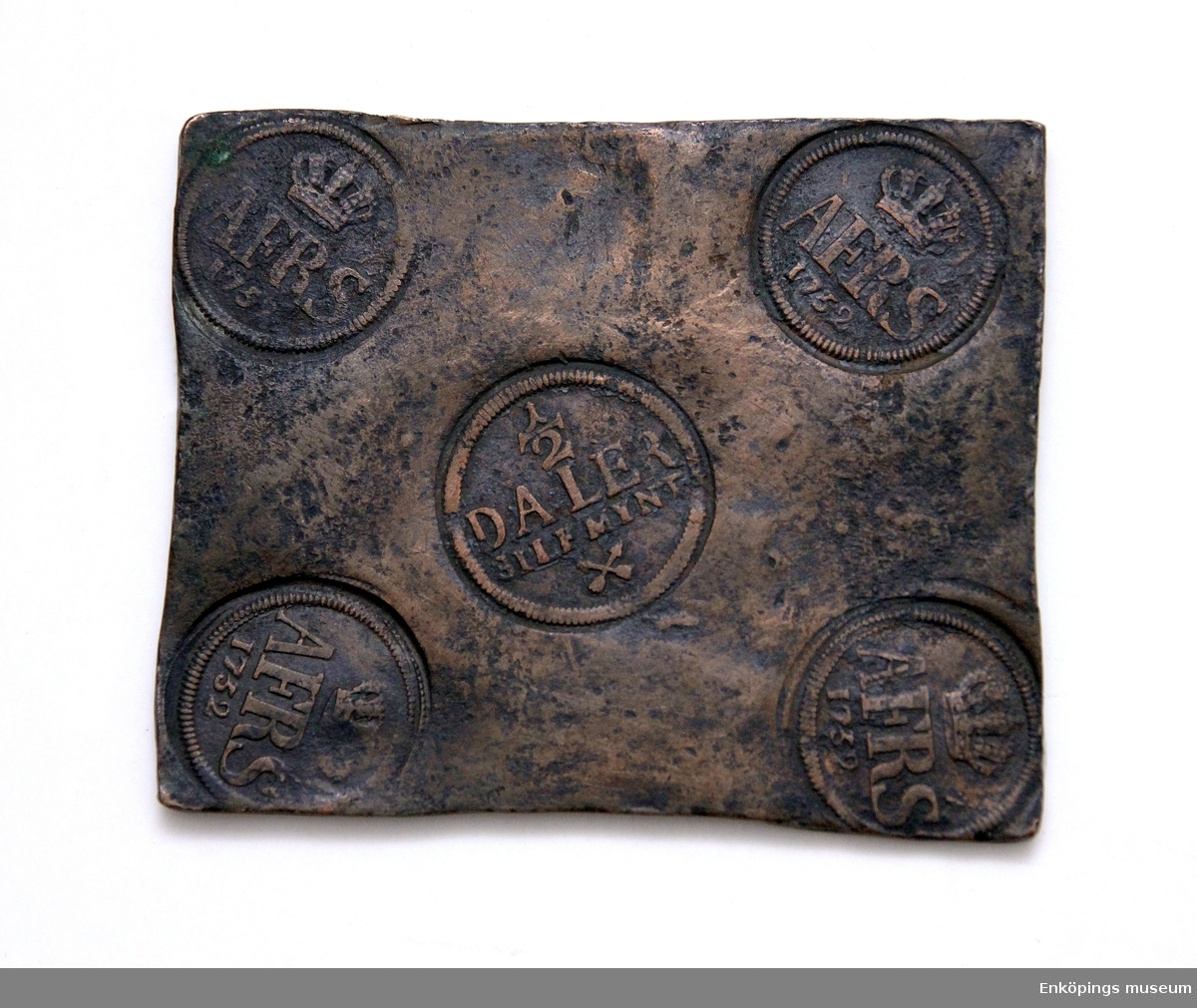 Plåtmynt av koppar, myntet har två olika stämplar i hörnen finns stämpel med krona följt av bokstäverna AFRS och årtalet 1752, AFRS= Adolf Fredrik ( Rex Sveciae) svensk kung 1751- 1771. Stämpel i mitten på myntet 1/2 DALER SILFmynt, två korslagda pilar.