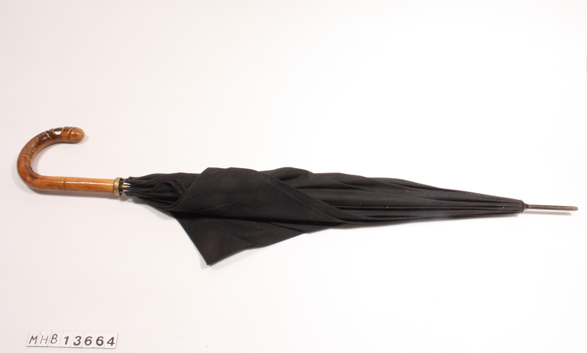 Sammenleggbar paraply uten trekk, med buet trehåntak og metallavslutning. Skjermen består av et ensfarget, svart stoff.
