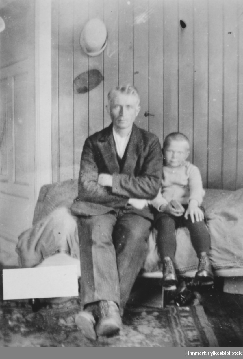 Andreas Sivertsen og sønnen Sivert sitter på en seng. Bildet er tatt i kammerset i våningshuset på gården Veines, Øvre Neiden
