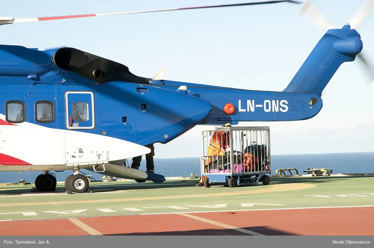 Helikopter av typen Sikorsky S-92A har landet på Valhall QP, og helikoptervakt Harry Buschmann er i ferd med å hente ut  bagasjen fra lasterommet i bakkant.