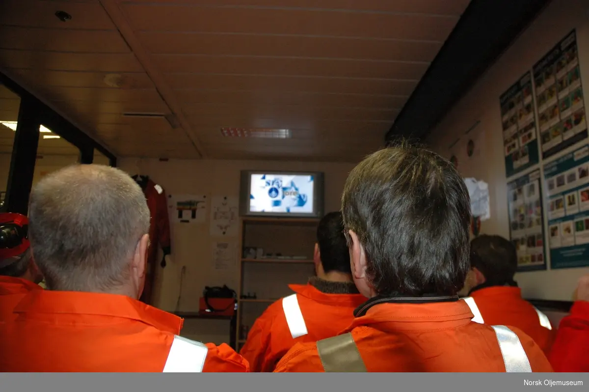 En gruppe mennesker ser på en presentasjon på en tv i et møterom på flotellet "Safe Scandinavia" i forbindelse med oppussing av plattformen.