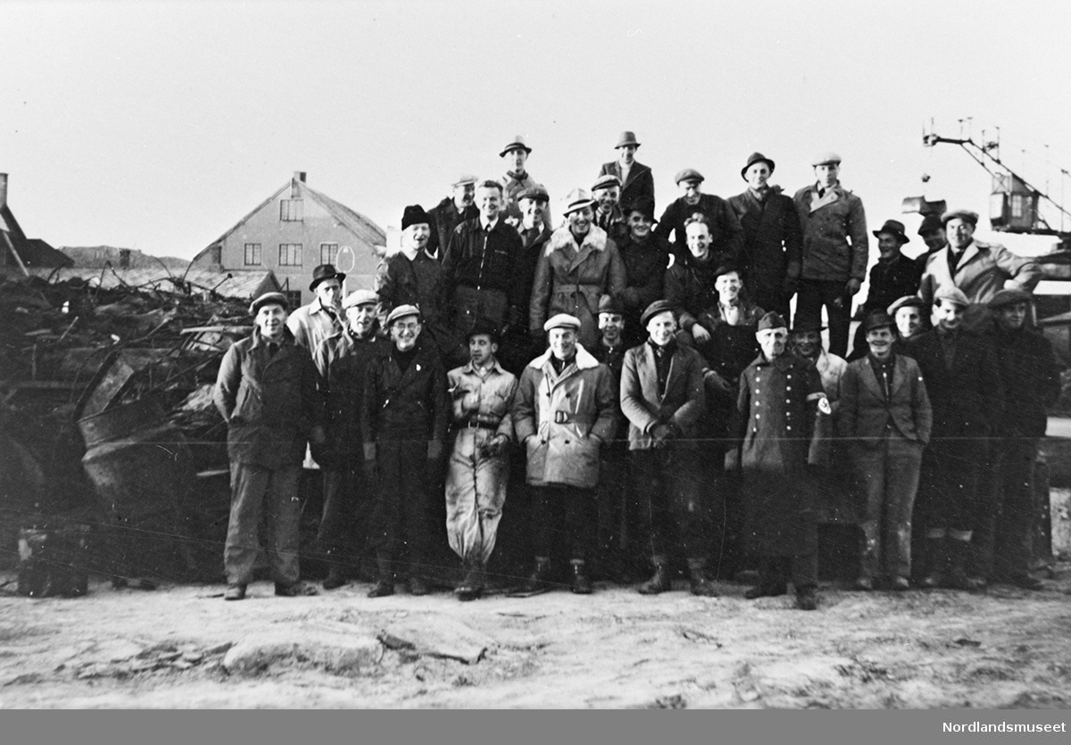 Gruppebilde. En gruppe mennesker oppstilt ute. Litt av kullkranen til Chr. A. Jakhelln t.h. Person nr 5 fra venstre er ikledd en tysk uniform med hakekors på høyre arm.