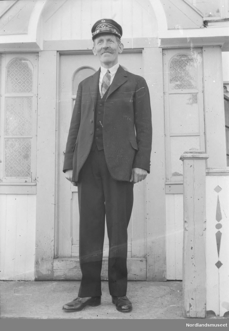 Portrett av mann stående på trapp foran inngangsdøren. Pent kledd.