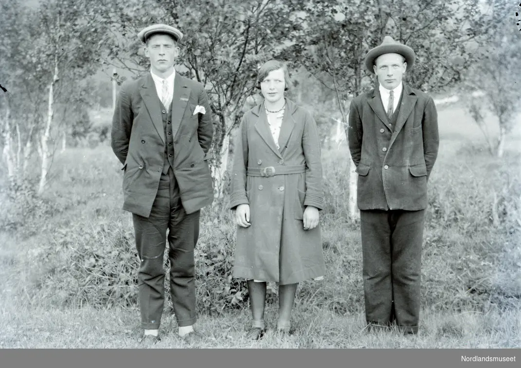 Portrett av to menn og en kvinne i midten. Pent kledd. Trær i bakgrunn.