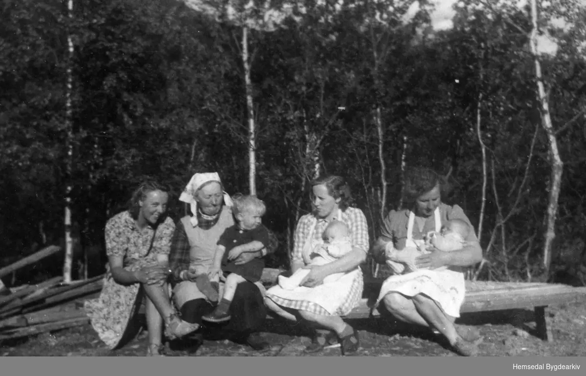 Frå venstre: Birgit Hennum, gommo Anne O. Tuv med Syver Tuv, fødd 1945, på armen, svigerdotter Oline Tuv med Anne Tuv, fødd 1947, på armen; svigerdotter Birgit O. Tuv med Syver Olav Tuv, fødd 1947, på armen.
Biletet er teke på stølen Fossen (Føssen).