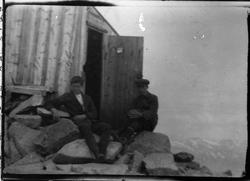 To menn sittende foran en fjellbu, fra pakke merket Arstal. 