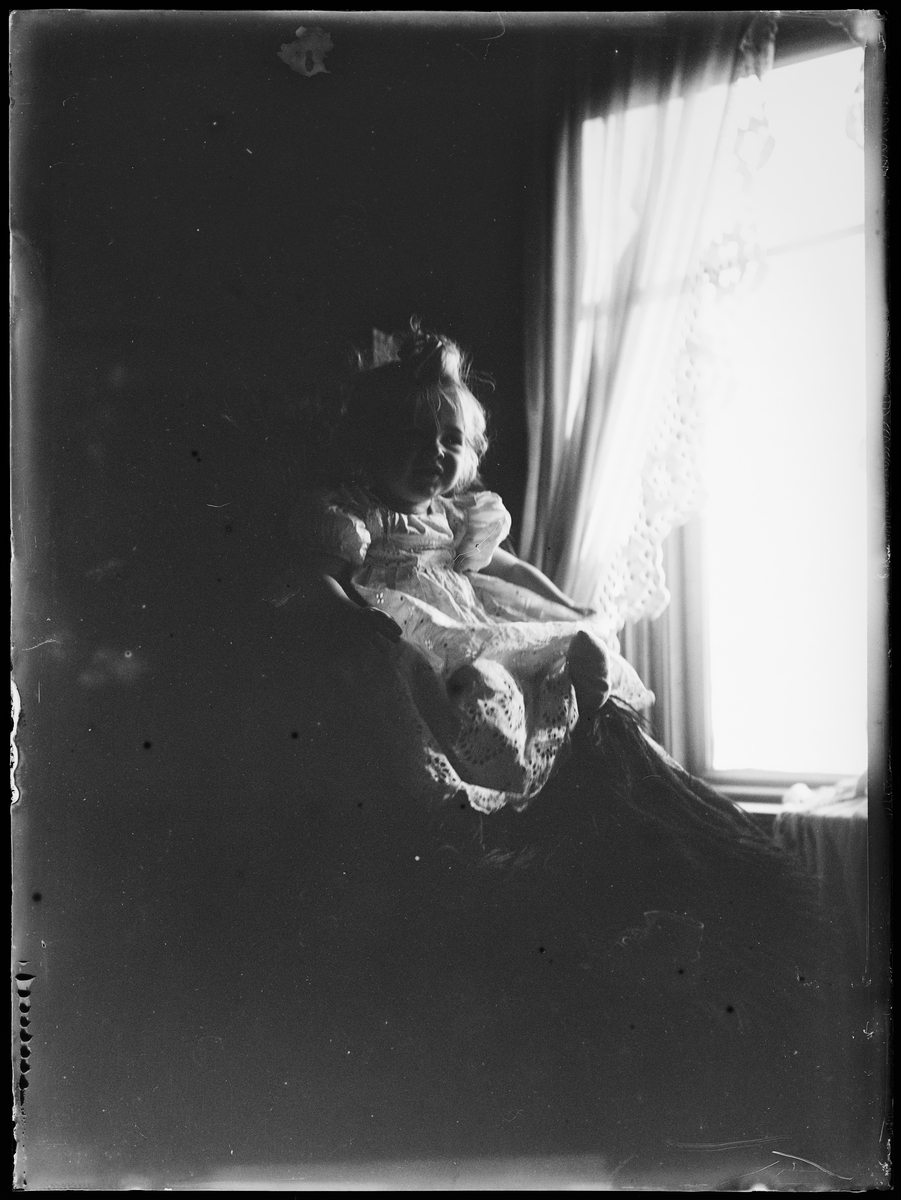 "4 mislykkede Billeder Arne Emil" (inskr eske). Et barn i lys kjole sitter ved vinduet.