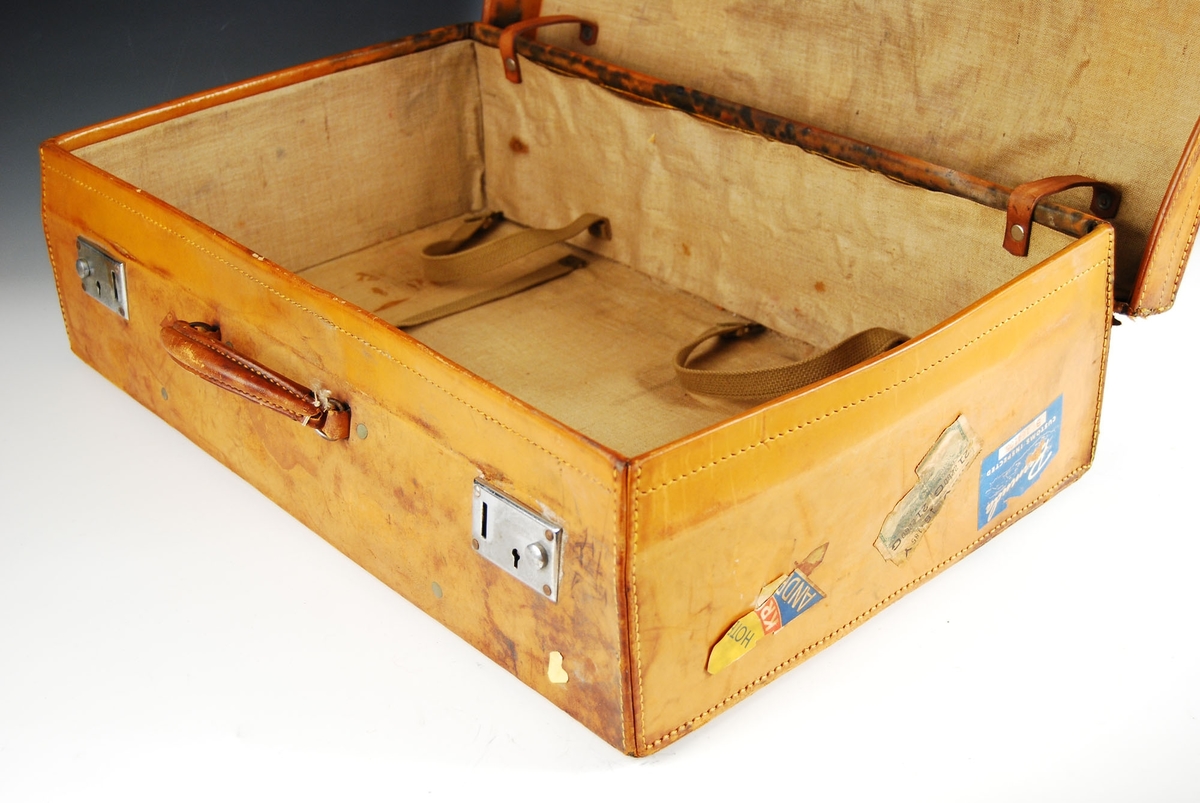 Koffert med to metallåser og håndtak av lær. Striefôr innvendig. 

Utvendig er det festet ulike klistermerker fra flere steder i verden.