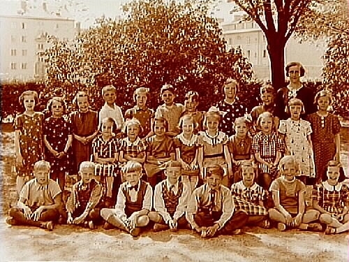 Engelbrektsskolan, 26 skolbarn med lärarinna fröken Emmy Söderlund (vikarie för Nilsson), sal 14.
Skolbyggnader i bakgrunden.