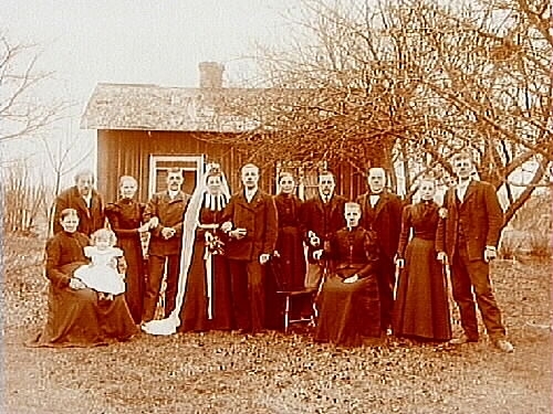 Bröllop. 13 personer.
Bostadshus, enkelstuga i bakgrunden.
Carl From.
Brudparet heter Erik och Augusta Granberg (De bodde i Granbergsdal, Almby socken fram till 1922 och sen på Hagvägen 24, Almby).