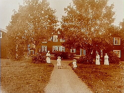 Berga gård, en och en halvvånings bostadshus med takhuv, 2 st. flygelbyggnader.
7 personer framför huset.
Albin Karlsson