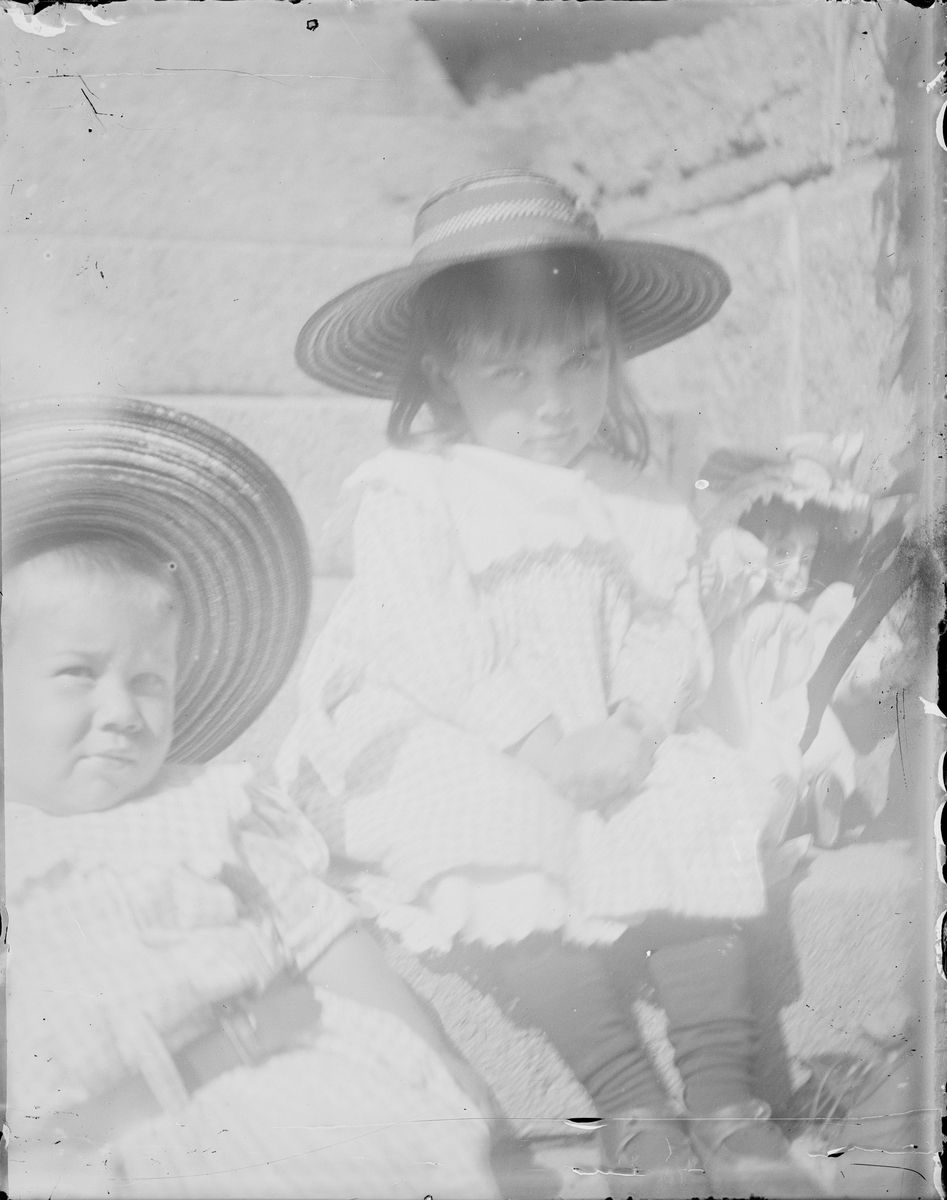To barn sitter på en steintrapp. Den ene sitter sammen med en dukke.