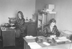 To damer sitter ved hvert sitt skrivebord. De er Randi Simon