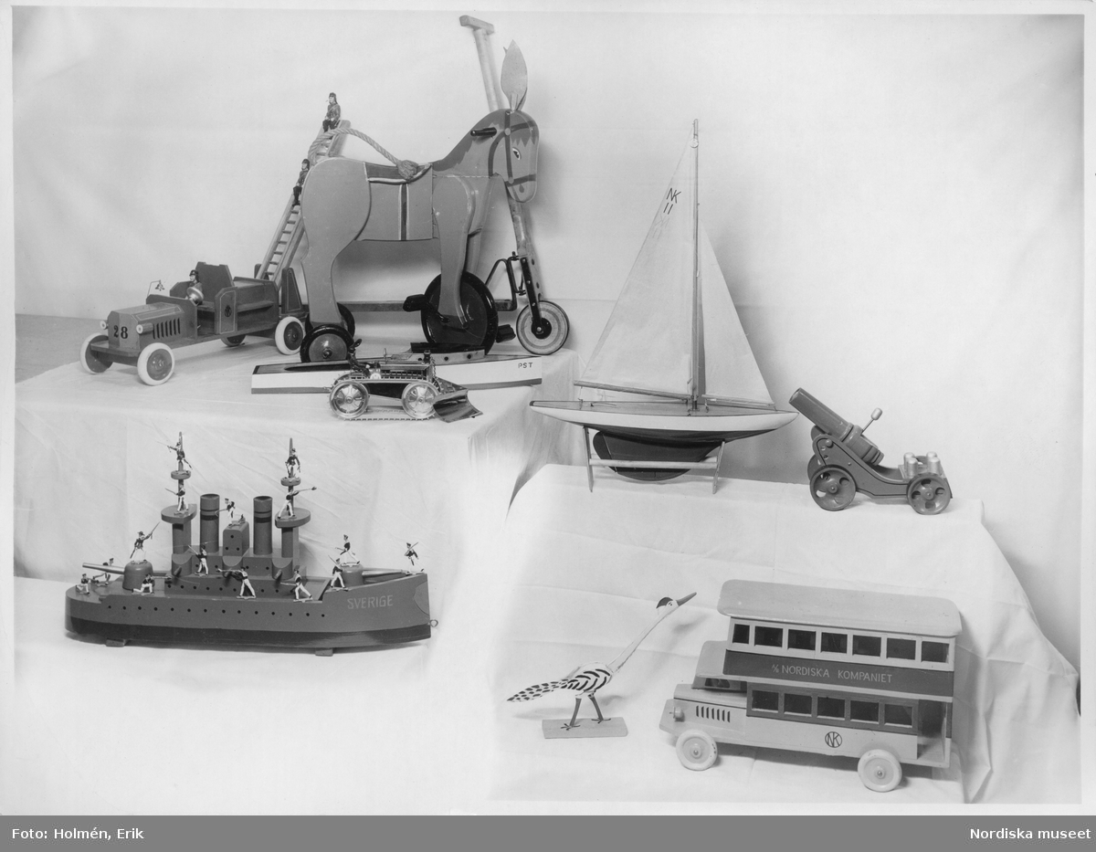 Nordiska Kompaniet NK. På tygtäckta podier står olika leksaker. Båtar, bil, buss, åsna, en kanon och annat.