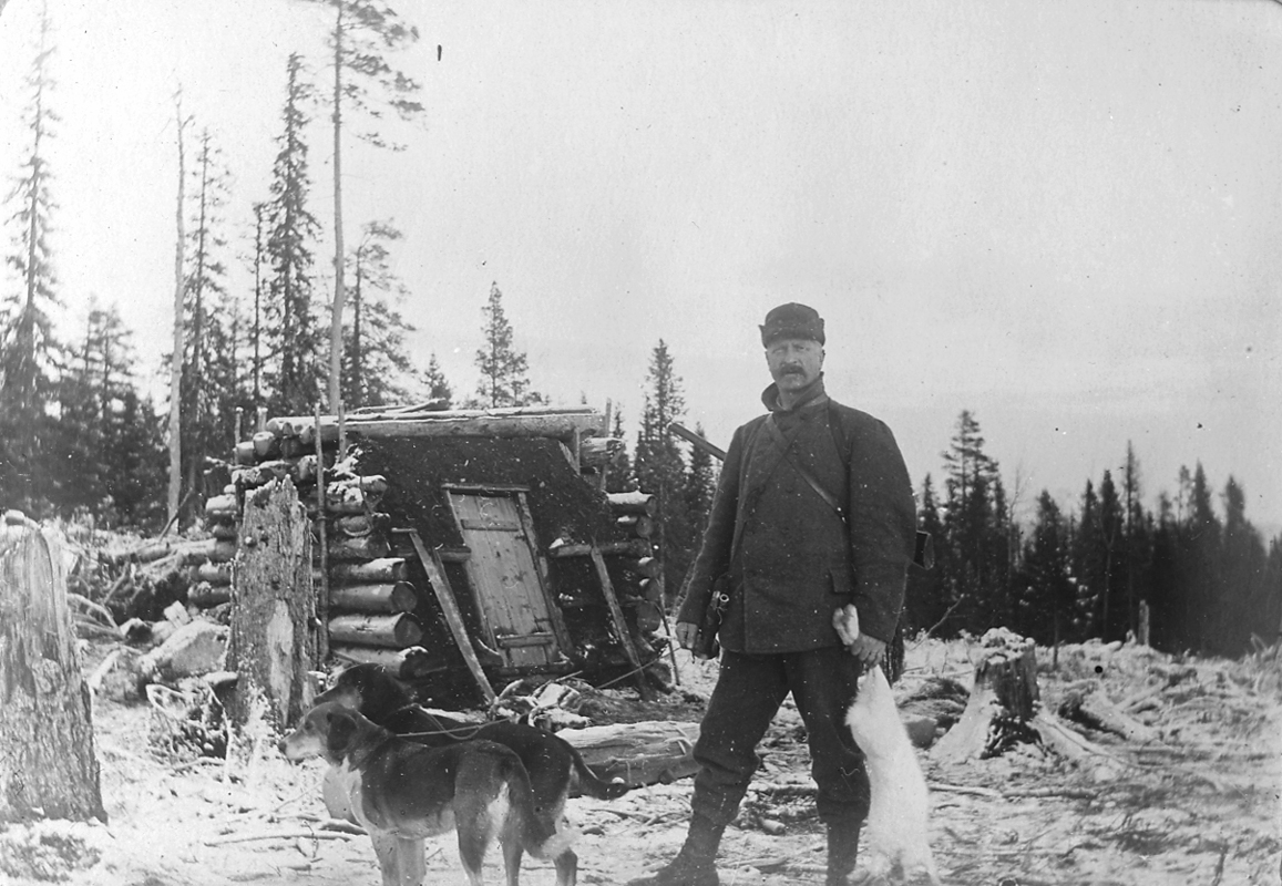 En man, jägare med två jakthundar och en kanin i handen.
Kolarkoja.