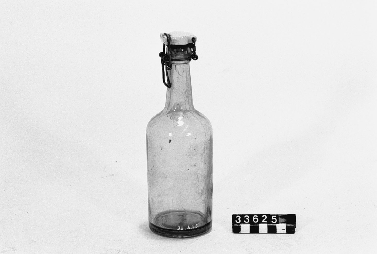 Flaska med patentkork, av svagt blågrönt glas, porslin och järntråd, med plan botten och en rymd på c.a. 35-37 cl. Avsedd för kolsyrade läskedrycker.