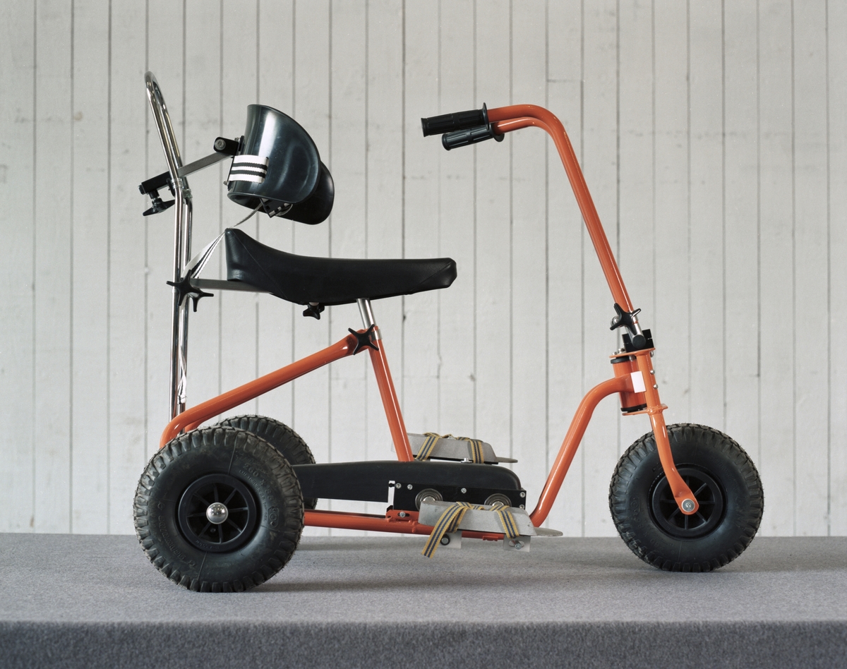 Handikappcykel avsedd för barn, gjord av gummi och stål. Standardutrustning: fotplattor, stödbåge, limpsadel och fotremmar m.m. Fällbart styre och luftgummihjul.