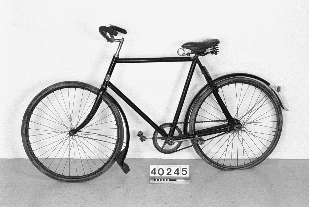 Cykel utrustad med blockkedja, med stänklapp av läder. Nummerskylt 184011. Cykellås: Reina. Skärmarna randade med guld. Ringklocka på styret. Mycket troligen nytt, t.ex. skärmar, styre, sadel och bakhjul.