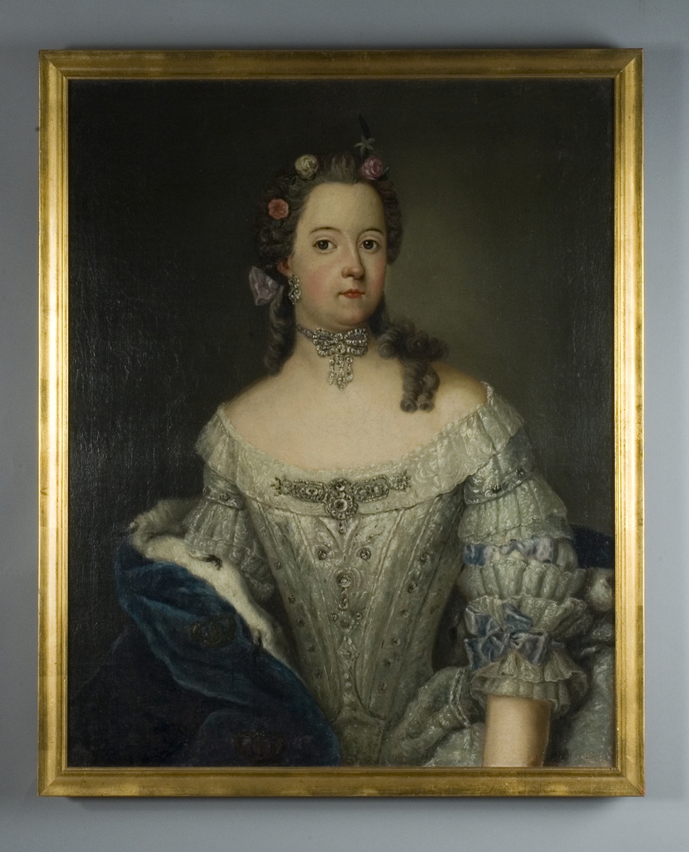 Porträtt av prinsessan Sofia Albertina, midjebild, klädd  i urringad vit sidenklänning med halvlång 
ärm med spetsar och band; blå hermelinsbrämad mantel över h. armen. Tätt sittande halssmycke och örhängen; blommor instuckna i håret, lockar över v. axeln;  rosett i nacken.
