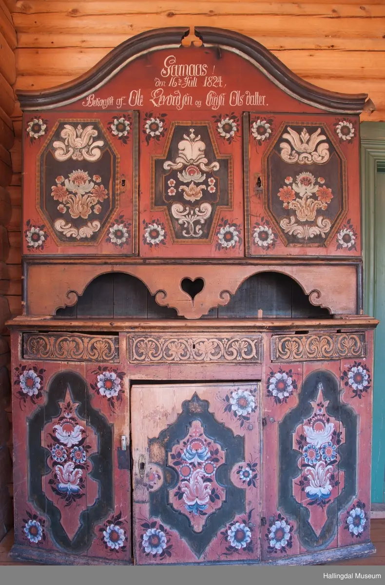 Delene festet med trenagler.  Høy, buet gavl med fremspringende kronlist som øverst har gjennomskåret omvendt hjerte.  Kronlist har hulkil og vulst, og fortsetter på sidene av overskap.  Overskapets front delt i tre felt, med en dør i hvert sidefelt.  Dørene er hengslet til skapets sider.  Hengslene av jern og festet på overkant og underkant av skap og på overkant og underkant av ramme.  Dørene har to profilerte labanker i spor på innsiden.  Låskasetter innfelt i dørblad.  Låsskiltene mangler.  Nøkkel med kløverformede hoder, profilert. En skillevegg midt i overskapet.  To hyller i hvert skap.  Dørene og midtfelt har speil med fyllinger og utskjæringer, akantus i relieff på speilflatene.  Dørspeilene er ovale, åttekantede.  Speil i midtfelt har tilnærmet korsform.  Skjenken har utskåret forplate, i tunger.  Under midfelt får forplaten helt ned til skjenkeplate med gjennombrutt hjerte.  Halvrunde åpninger i hver side. ..........