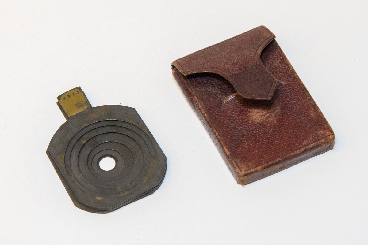 Gruppering med fotokamera i oppbevaringskasse, separat metall-lokk, stereolinse, lause delar som negativplate, mattskive, blendarsett og diverse smådelar.