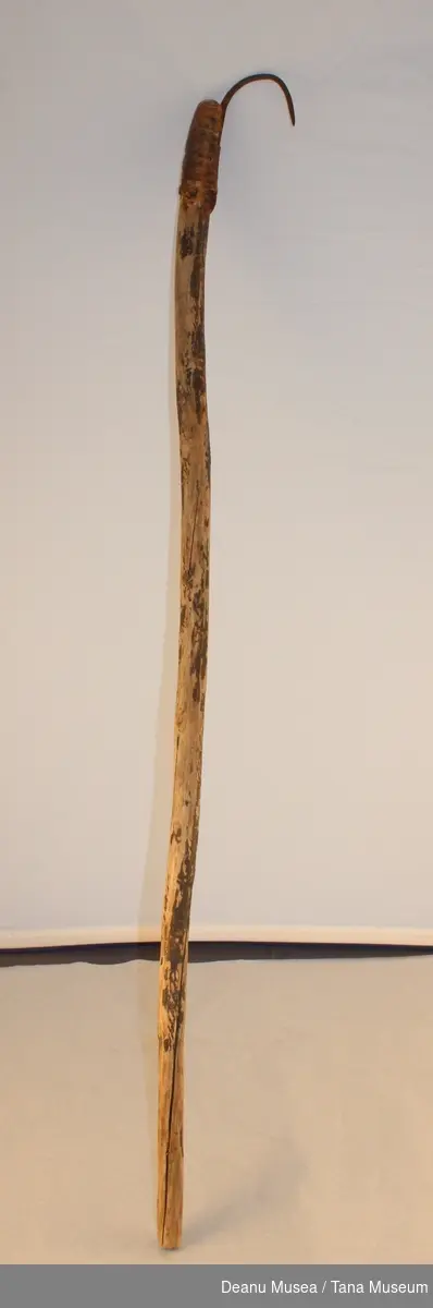 Tradisjonell hjemmelaget lang lakseklepp. Treskaftet er laget av en lang grein. Stålkroken er limt fast med hampsnøre/tau og malt over tauet med brun maling eller lignende.