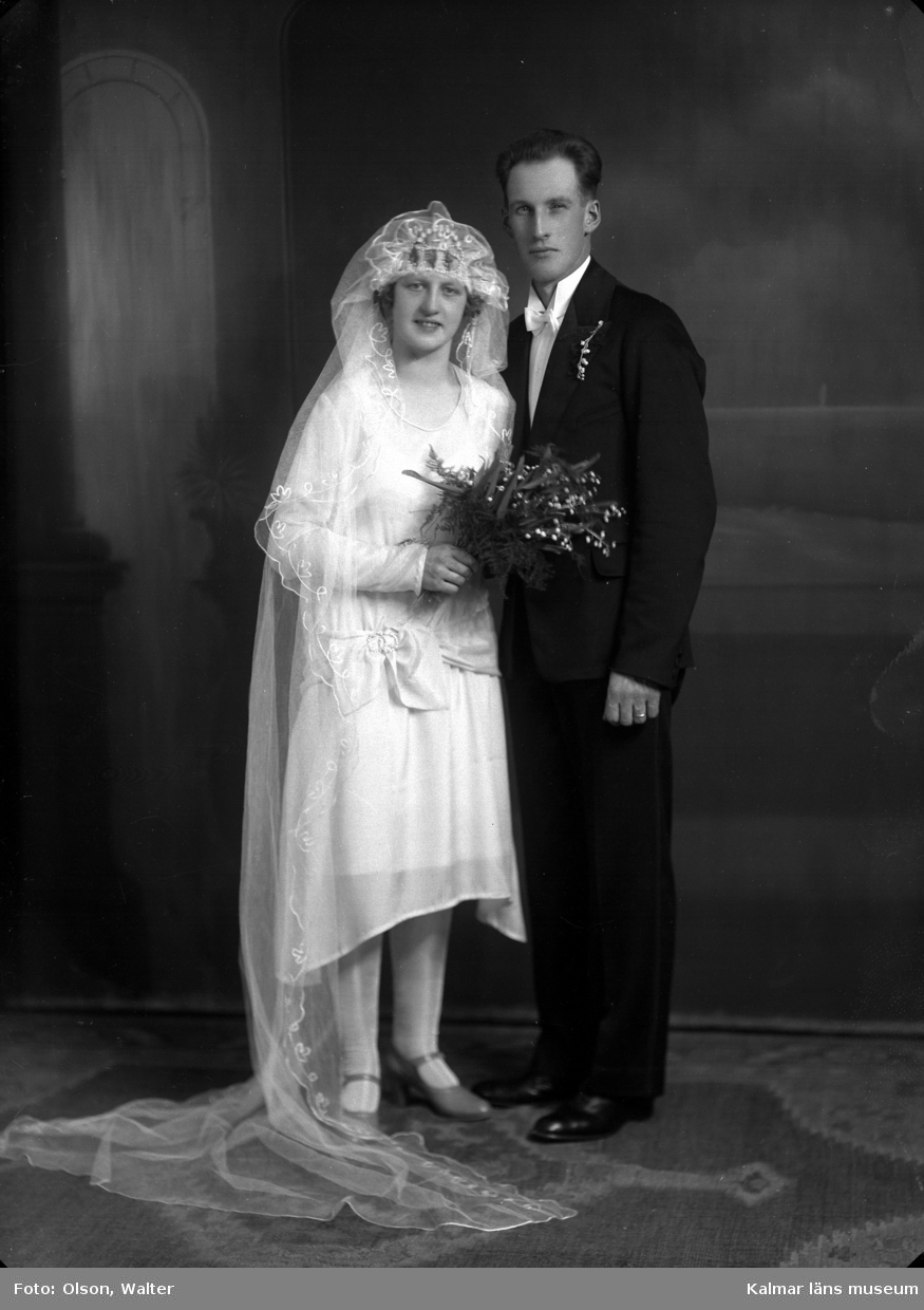 Bröllopsfoto av ett par. Kvinnan har slöja och håller i en blombukett. Mannen har kostym. Enligt Walter Olsons journal är bilden beställd av Artur Johansson ifrån Lindölundsgatan 14 i Kalmar. Kalmar läns museum känner inte till om det är den personen som är avporträtterad.
