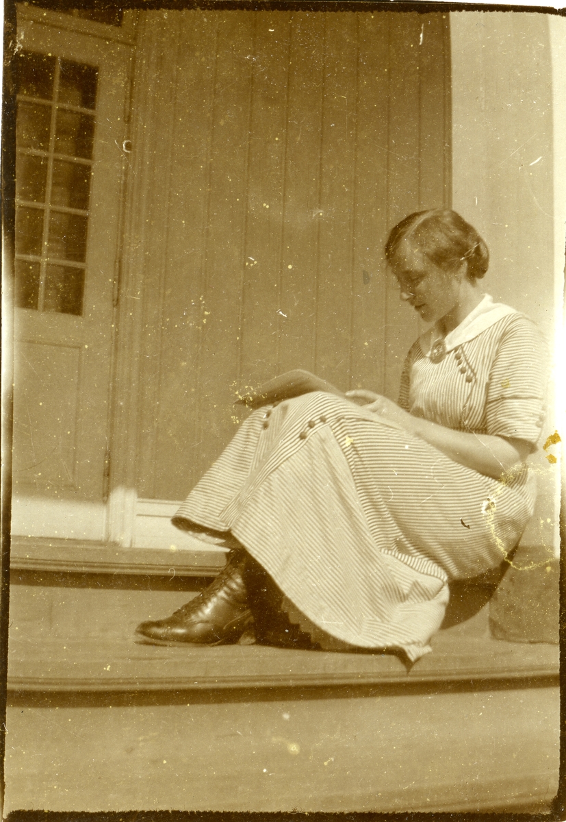 En kvinne sitter på en trapp og leser. Kvinnen er iført kjole og støvletter.