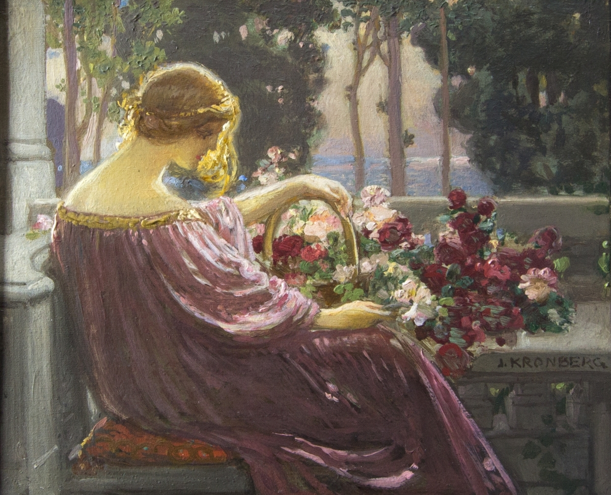 Ung kvinna sittande på en veranda klädd i rosa klädnad med ryggen mot åskådaren. Framför henne ett bord med blommor och en korg med blommor. Kvinnans ena hand vilar på korgens handtag. I bakgrunden träd och sjö.