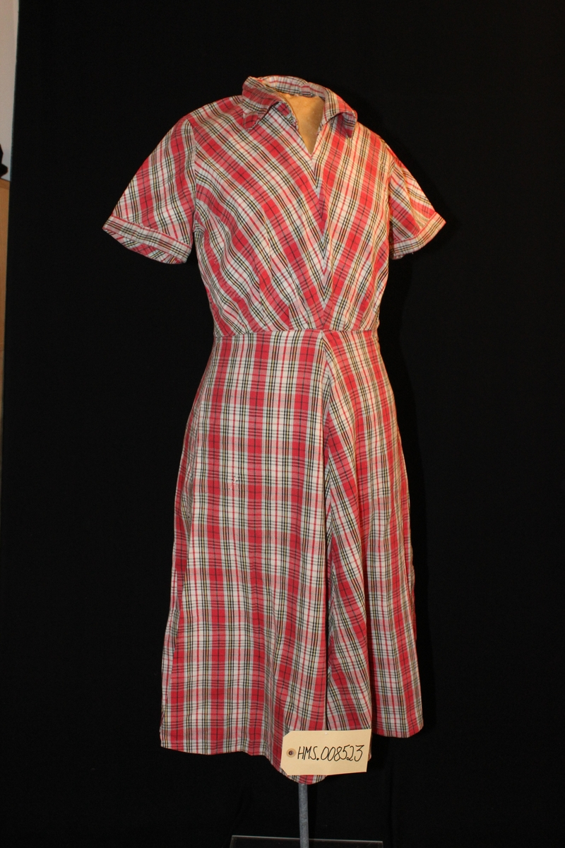 Rutet kjole rød med liten arm, trykk knapp på den ene siden. Pynteknapp på kraven i samme mønster som kjolen.