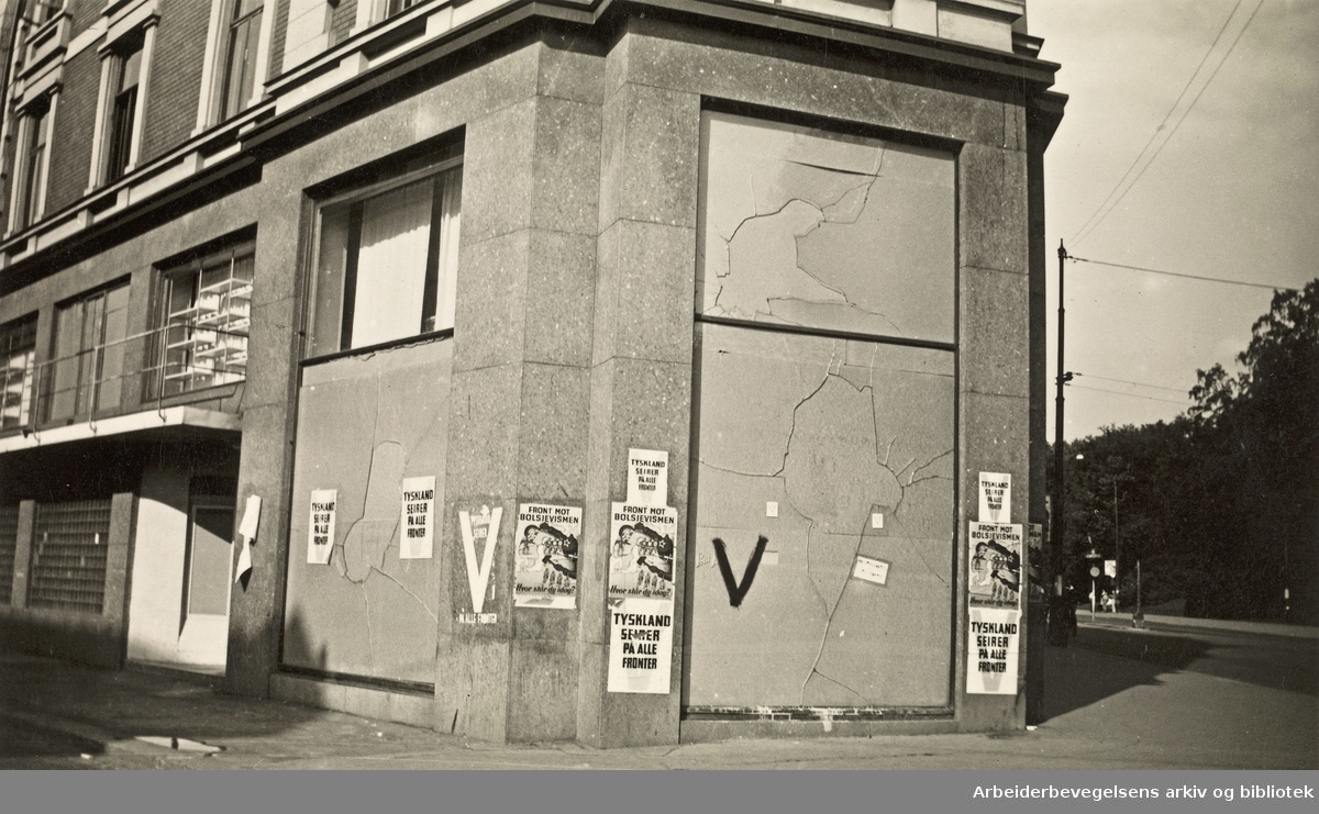Ole M. Engelsens fotografier fra okkupasjonsårene i Oslo..Bygård på hjørnet av Drammensveien og Kronprinsens gate. Plakater med "Tyskland seirer på alle fronter" og "Front mot bolsjevismen - Hvor står du i dag?".Foto 27 juli 1941.