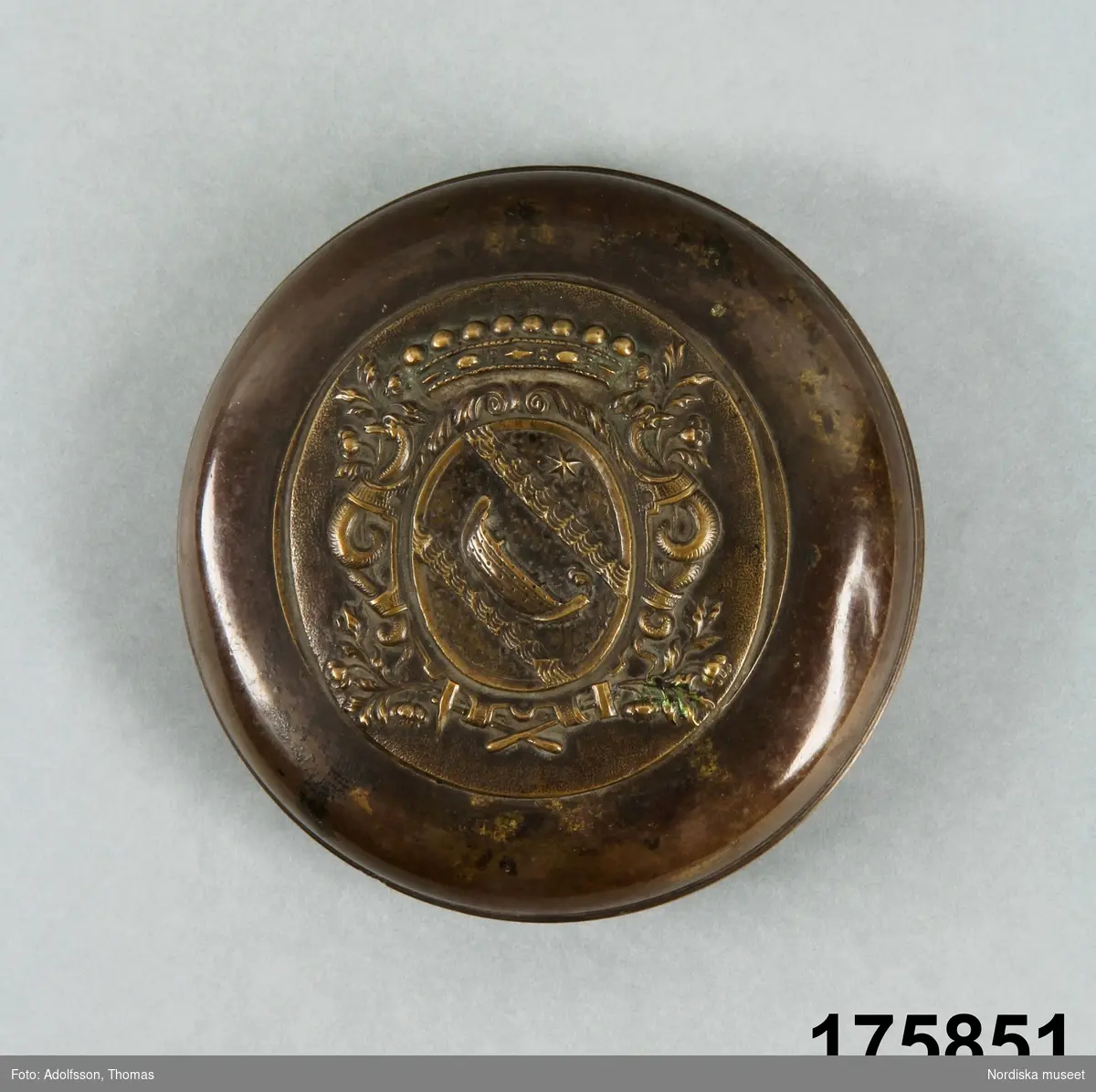 Dosans lock med hjärneska vapnet (båt under stjärna), reliefdekor med sjöhästar mm. Medalj med profilporträtt i relief.