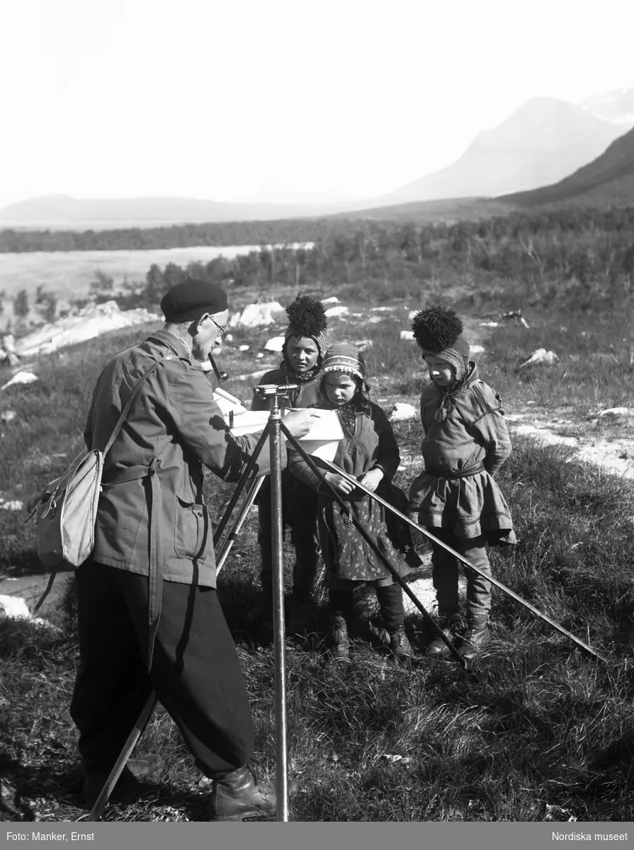 Harald Faith-Ell kartlägger vistet vid Vaisaluokta. Tre små barn i samisk dräkt tittar nyfiket på.