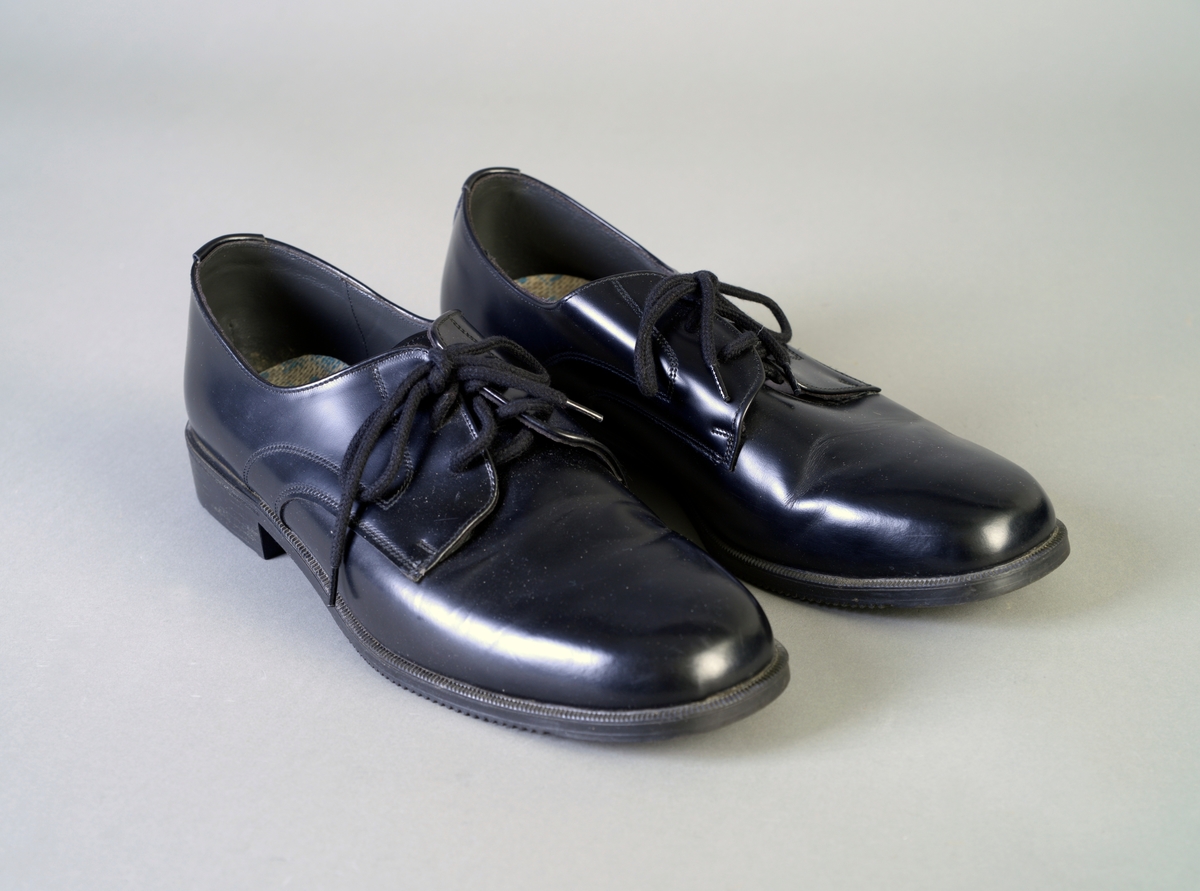 Et par svarte sko med overdel av svart lær/skinn og såle laget av gummi. Skoene har knytting, og lissene er laget av bomull. Det har vært et produksjonsstempel i høyre sko, men det er for slitt til å tyde. Begge skoene har innelggssåler (som er nokså slitt). Sålen har  mønster i ruter og striper under.