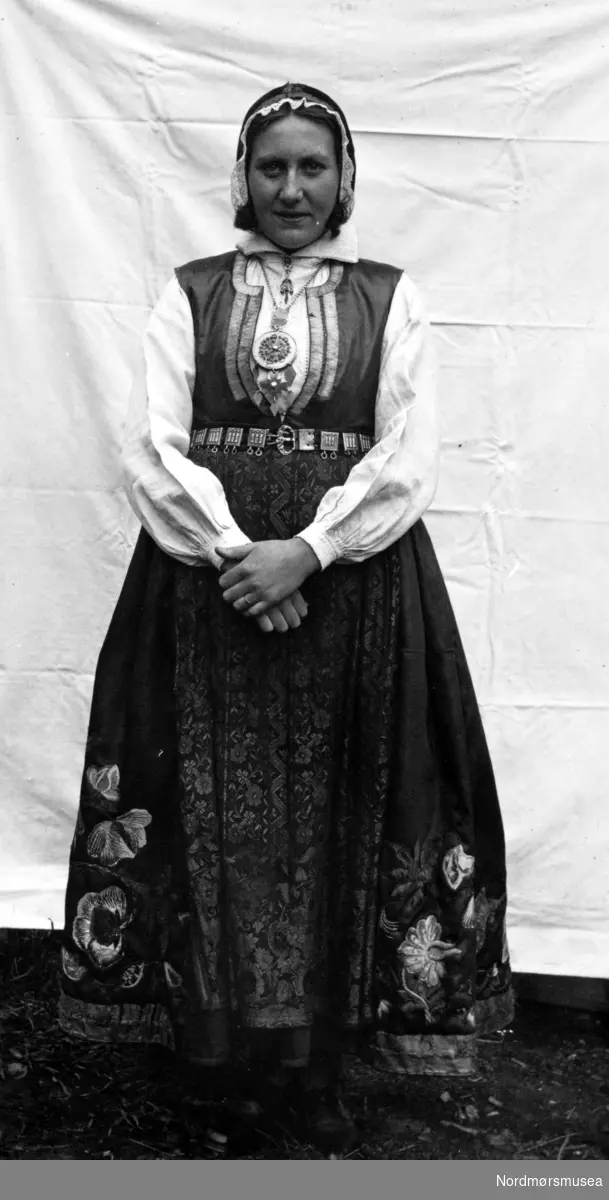 Kvinne fra Sunndal, iført deler av en brudedrakt, med belte, sølje, lue med mer. Datering mangler. Fra Nordmøre Museums fotosamlinger.