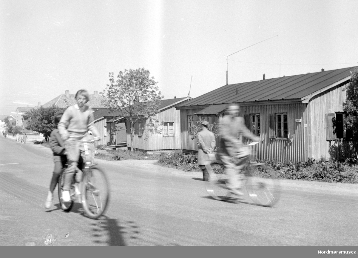 På bildet ser vi brakkene i Langveien, fotografert nær skillet ved Kaasbølsvei, med to syklister i forgrunnen. Bildet er datert 1958. Fra Nordmøre Museums fotosamlinger.
