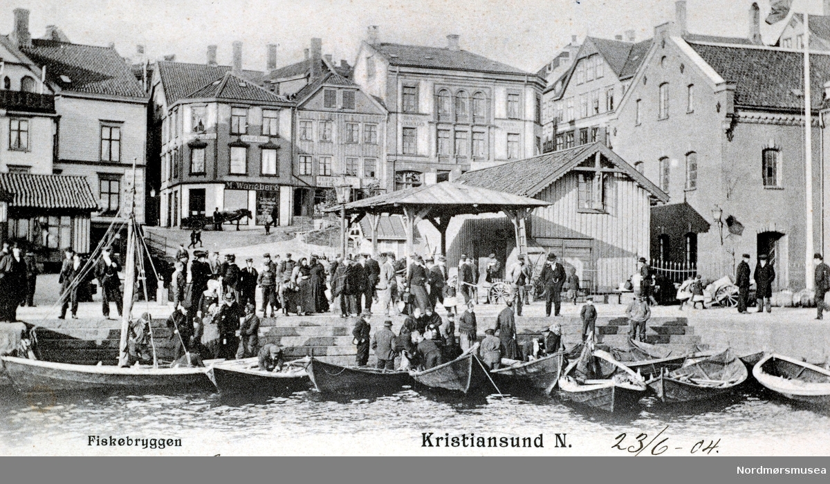 Postkort datert 23. juni 1904, hvor vi ser fra fisketrappa og fisketorget på Kirkelandet i Kristiansund. Her kommer de lokale fiskerne til fisketrappa for å selge dagens fangst. Vi ser også litt av Loennechens bokhandel til venstre, samt Tollboden med lagerbygning til høyre. Fra Nordmøre museums fotosamlinger. /Reg:EFR2013/



