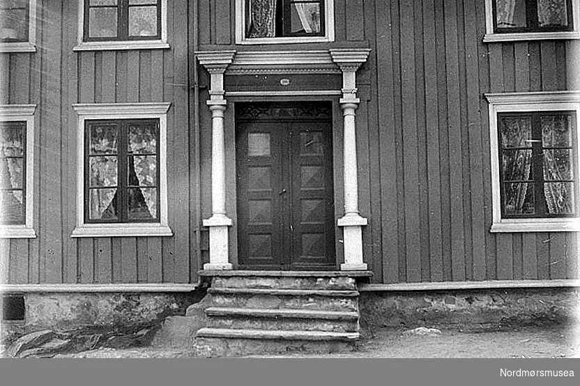 Gatedør til bolighus i Storgt. 51, matr. nr. 393 på Hålahaugen,  1912.
Huset eies av familien Løkke. Portalen er laget av tømmermann Simon O. Helland (d. 1852) straks etter Hålabrannen 1848. Han eide huset 1838-1852. dvs. han bygde det opp igjen. Enka Marit E. Hustad var eier fram til 1860. Vanlige fyllinger på dørbladene, flate på innsida. Glatte halvsøyler. Vinduene har ikke sidelister, men i stedet en hvitmalt stripe på bordkledningen.  Derimot har vinduene overlist og underlist (gerikt). Husets bordkledning er opprettstående med over- og underliggere;  overliggerne har en liten profil langs kanten.  --- 
Katalog over bilder av eldre gateparti, bygninger og bygningsdetaljer i Kristiansund. Bildene er bekostet av Det Kulturhistoriske Lag (DKL)og med bidrag av Kristiansund Sparebank og fru Caroline Knudtzon. Ført i protokoll av overlærer Wilhelm Lund. Foto hovedsakelig utført av fotograf Ole Olsen Ranheimsæter dersom ikke noe annet er anført. Tegninger utført av billedhugger J. Johnsen og Ole Ranheimsæter. DKL - er en forløper for Nordmøre Historielag, i tett samarbeid med Kristiansunds museum. Nr. 162 Portal til hus, matr. nr. 393 i Storgaten (paa Haalahaugen), Kirkelandet. Fot. for D. K. L. 1912. Huset eies av en mand ved navn Løkke, og er et mindre hus. Hurderne har de sedvanlige mot midten ophøiede firkantede fyllinger. De øverste fyllinger er vistnok i allerseneste tid erstattet av ugjennemsigtlig glas. Paa hurdernes indside er fyllingene flate med profilerede kanter. Over hurderne er et vindue med dekorativt listverk. Døren omgives av følgende dekorative dele: Halvsøiler med kapitæl og basis hvilende paa postament; kapitælens abakus er tyk og firkantet, og paa samme abakus staar en kort, firkantet støtte; der over en forkroppet og profileret gesims med en rad av ruter (ikke tandsnit) nedentil i et 3-ledet baand lignende den joniske arkitrav gar et stykke over abakus forbindende de to korte, firkantede støtter. Søileskaftet smalner av opad og nedad; det er ikke kaneleret. Søilens basis har hulkil mellem to vulster. I fig. 1. sees en skisse av kapitælen og øverste del av søileskaftet. Fig. 2 er en skisse av søilens basis og postamentet, og fig. 3 viser en skisse av det 3-delte baand som forbinder de korte, firkantede støtter over abakus. Det bemerkes at kapitælet har tyk, firkantet abakus og doriskaftet echinus med en enkelt profil nedentil. Søileskaftet har en ring rundt halsen. SKISSE: VI Samme hus har paa en del av vinduerne ingen sidelister, men i stedet herfor kun en hvitmalet stripe paa bordklædningen. Derimot har vinduerne overlist og underlist (gericht); disse sidste lister sees paa billedet. Husets bordklædning er opretstaaende med over- og underliggere; overliggerne har en liten profil langs kanten. I. L. Fortæller 1912 om denne portal: "Denne portal kan jeg ikke huske annerledes end nu 1) Den er arbeidet av tømmermand Simen Helland. Denne mand var tømmermand her i Kristiansund. Dette vet jeg. Jeg kjendte denne tømmermand. Denne portal er opført straks efter branden i 1848; det husker jeg". 1) Formodentlig naar undtages ruterne i hurderne. (W. L.). Fra Nordmøre Museum sin fotosamling.