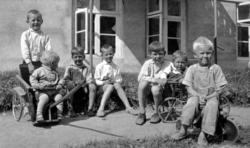 En gruppe med syv barn. Noen sitter i gresset og noen sitter