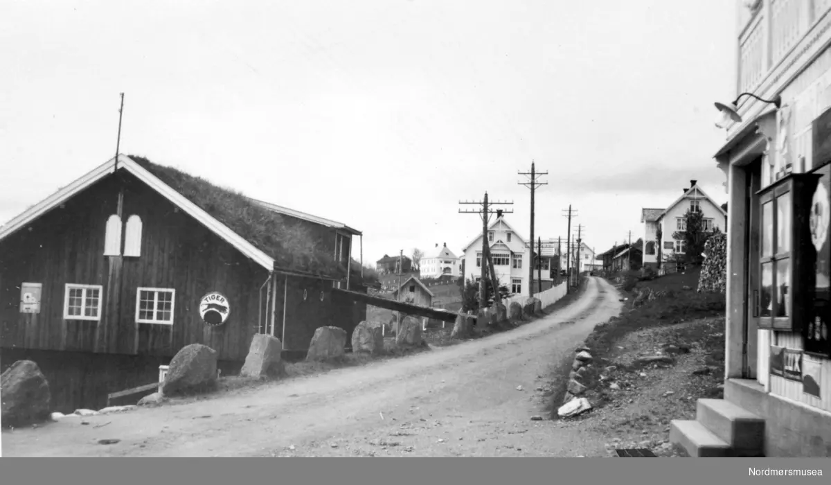 Bilde fra Kvenna (Kvanne) ";sentrum"; i Surnadal kommune. Fra venstre ser vi først en låve og deretter et bolighus. Til høyre ser vi først en kolonialbutikk og deretter posthuset. Serie. Fra Nordmøre Museum sin fotosamling
