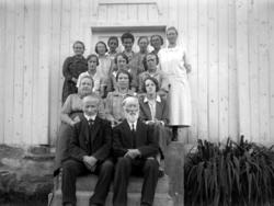 Foto av to menn og 13 kvinner på en trapp opp til en bygning