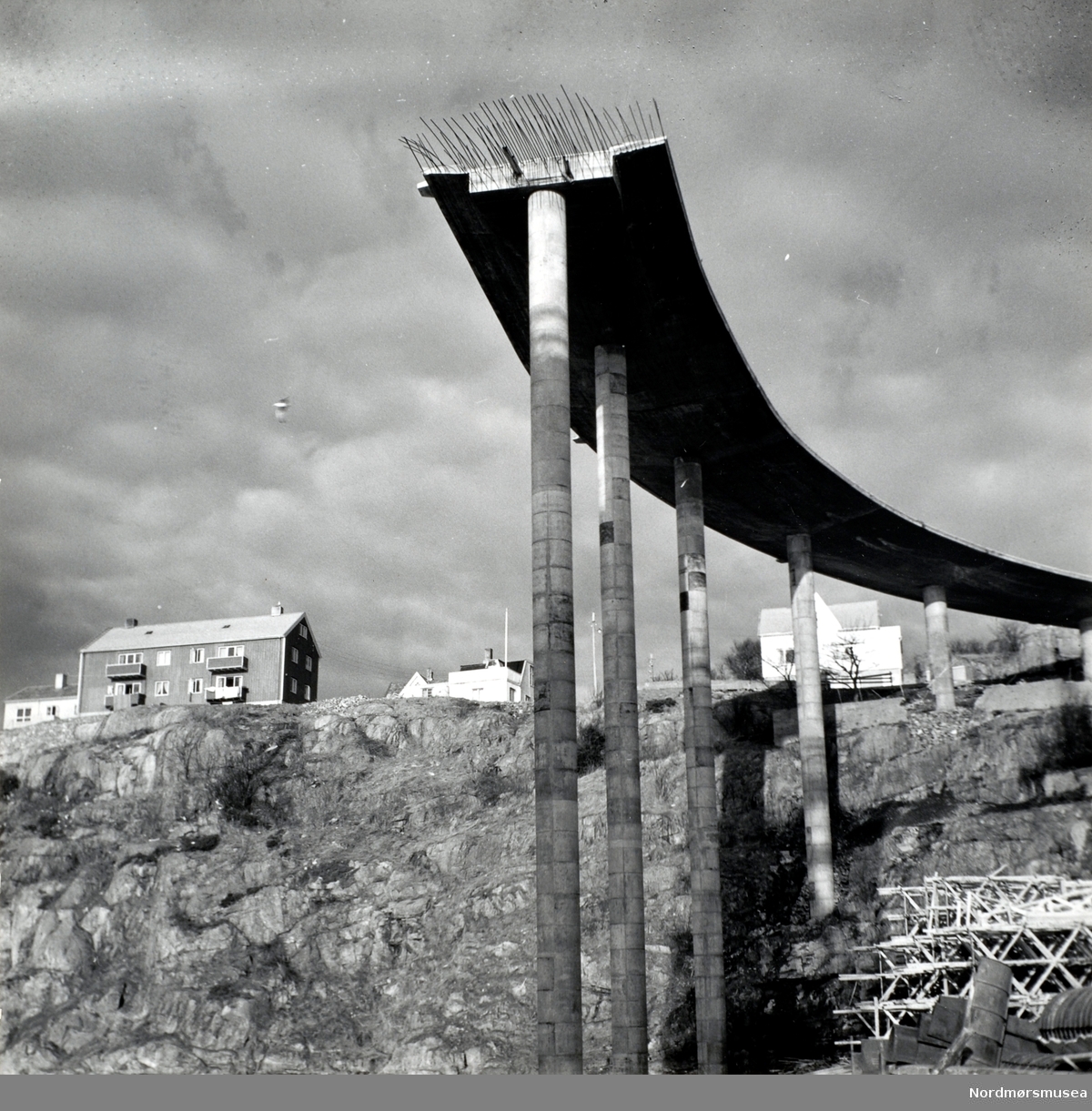 Foto fra byggingen av Sørsundbroen. Broen vil bli omkring 408 meter lang og 9,3 meter bred, med en fri høyde over vannet på omkring 39,6 meter. Broen vil veie bort i mot 10.000 tonn når den er ferdigbygd. Det er circa 50 meter mellom pilarene med 100 meter på det meste midt på, samt beregnet til et akseltrykk på 10 tonn. Broen stod ferdig omkring sommeren 1963.  Entreprenør var Vestlandsbygg A/S, og arbeidet ledes av firmaets sjef (per 17.02.62), sivilingeniør H. Nafstad. Kilde: Avis. Nordmørsposten eller Romsdalsposten? Lørdag 17. februar 1962. Fra Nordmøre museums fotosamlinger.